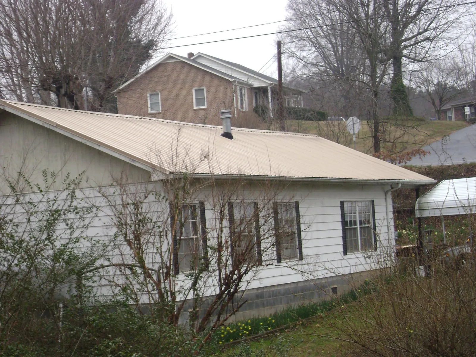 Tan metal roof on a white sided house set into a hillside in Newton
